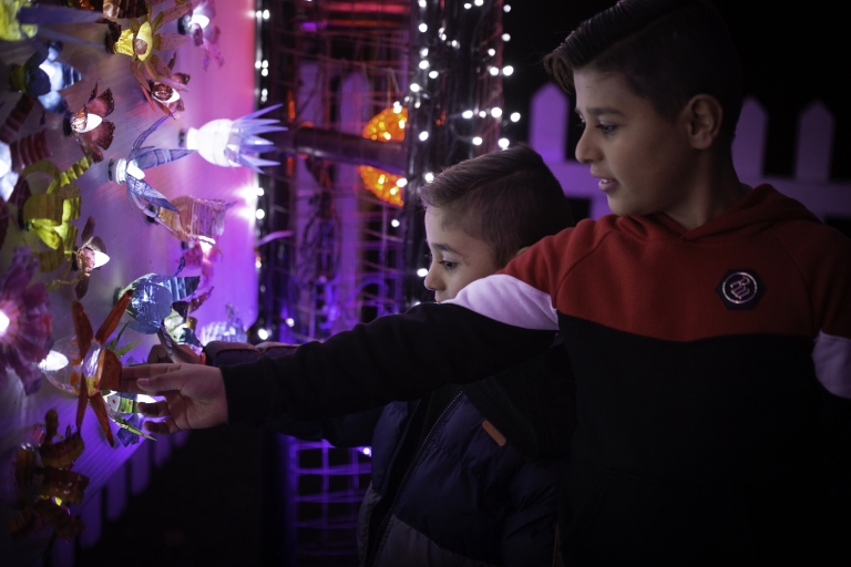 Two boys reach out to touch a display wall of lights and ornaments