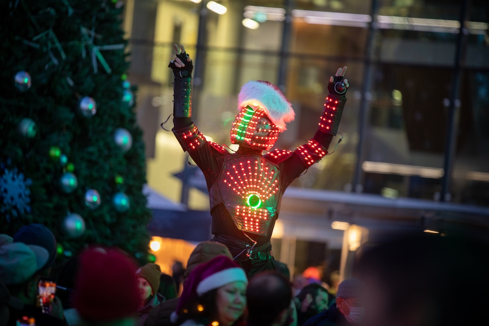 Stilt walker in costume make entirely of Christmas lights walks among crowd