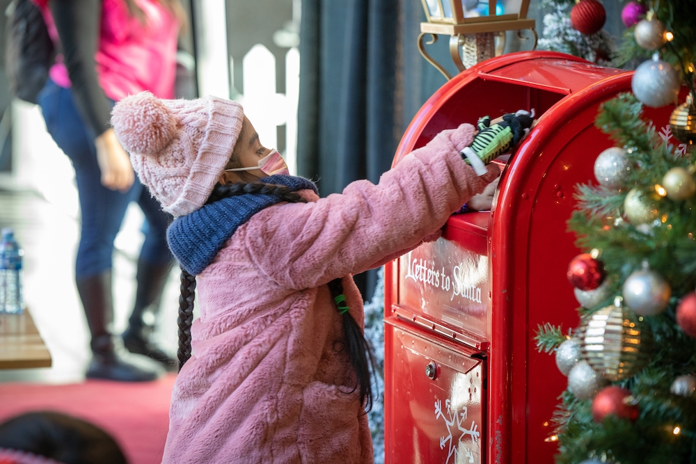 Little girl reaches up to put letter to Santa into special Christmas mailbox