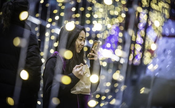 Young woman surrounded by Christmas lights takes photo with phone
