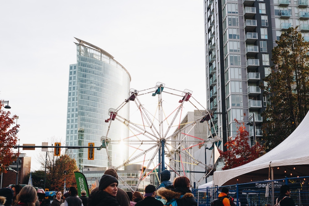 Festival crowd with ferris wheel and city buildings in background