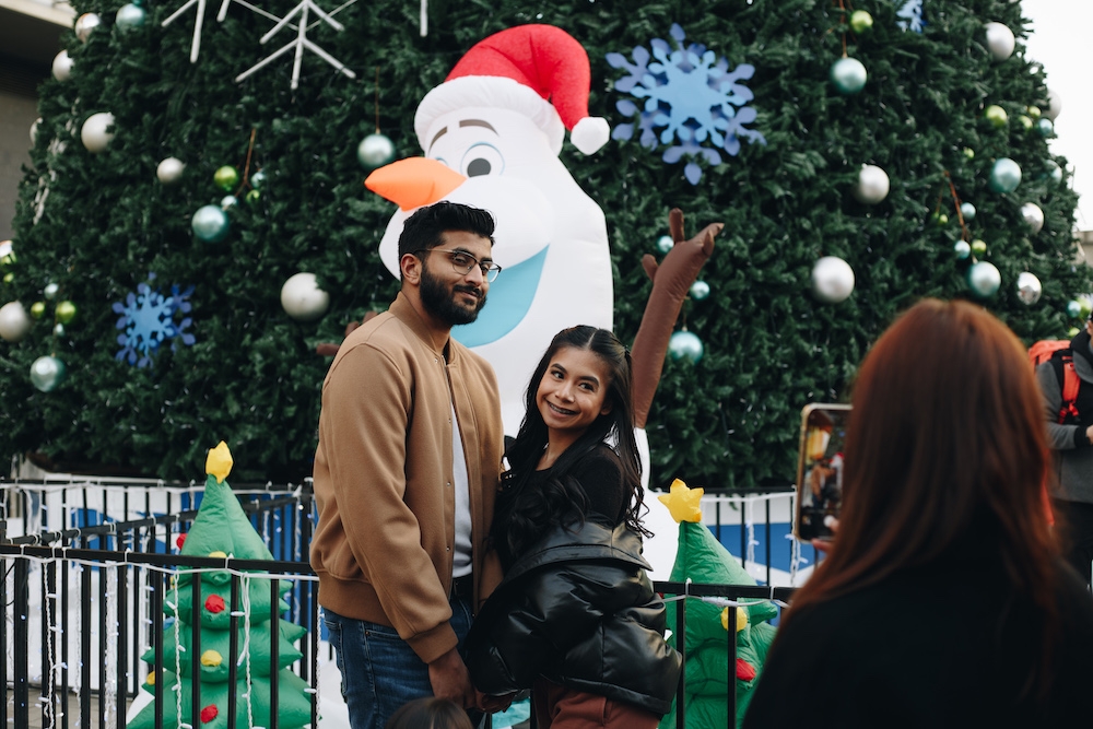 Young couple stand together for photo with large snowman decoration